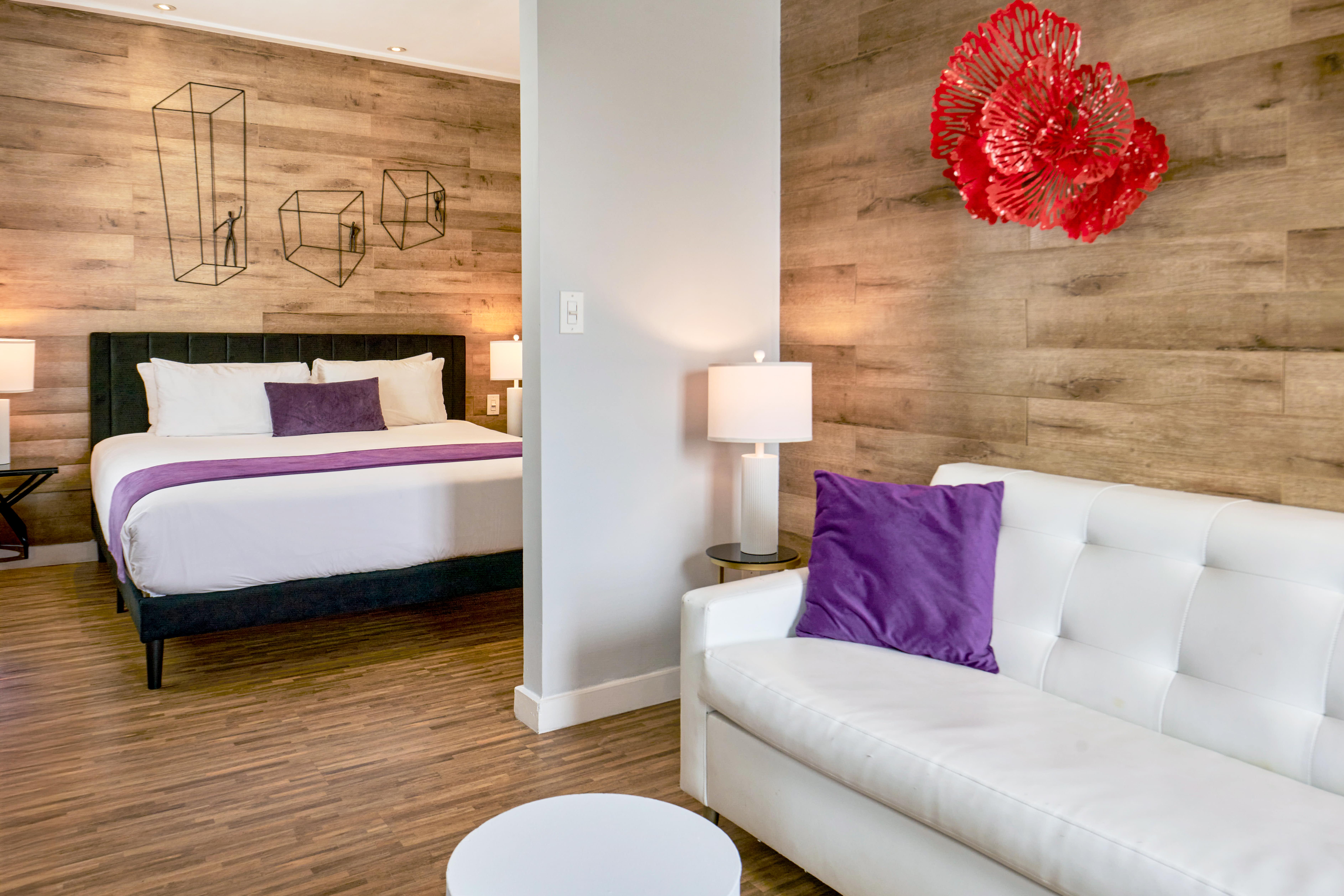 A hotel room with a white sofa, a bed with a black headboard, and a wooden wall with decorative art.